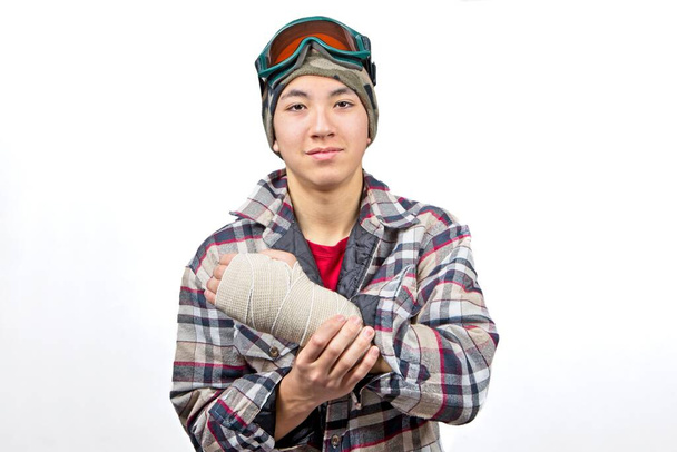 Portré egy tinédzser fiúról, aki bekötözve mutatja a törött csuklóját egy snowboard baleset után.. - Fotó, kép