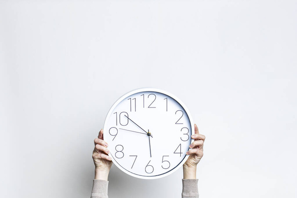 Manos femeninas sosteniendo un gran reloj blanco sobre un fondo claro  - Foto, Imagen