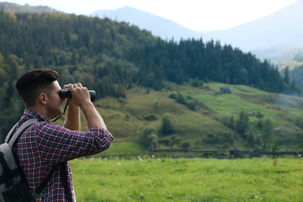 Man with backpack looking through binoculars in mountains - Foto, immagini