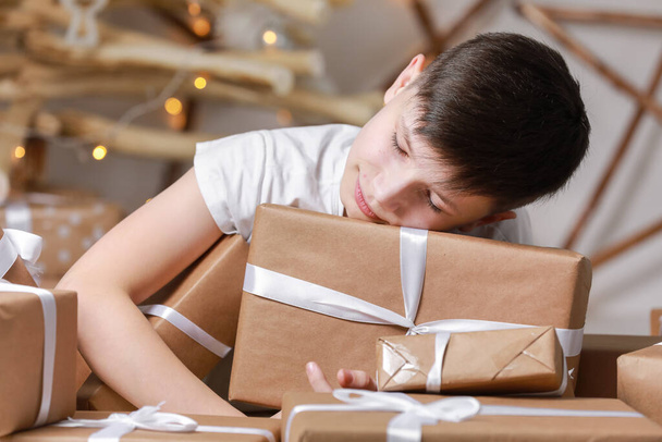 kid boy is sleeping on a lots of gift boxes by the decorated christmas tree. happy winter holiday vacation - Photo, Image