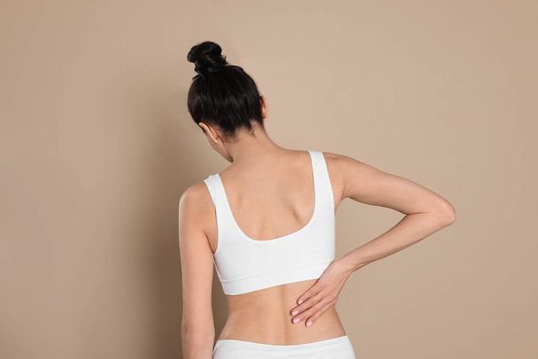 Woman suffering from pain in back on beige background - Φωτογραφία, εικόνα
