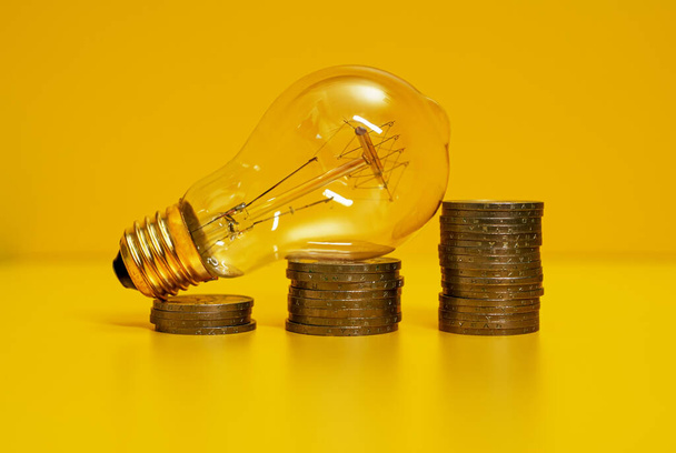 Concept of rising electricity prices. Lamp and coins. - Foto, afbeelding