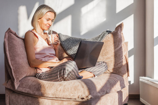 Happy dreamy middle aged woman sitting on sofa in living room with cup of tea or coffee, looking away, Peaceful adult lady enjoying no stress calm positive pastime alone at hom - Fotoğraf, Görsel
