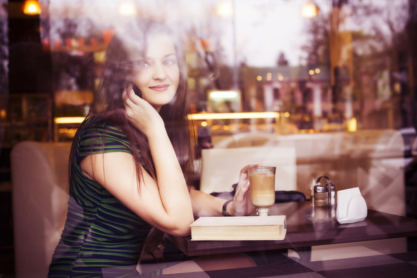 Femme brune assise au café lisant le livre, claquant et buvant du café et parlant au téléphone. Espace de copie
 - Photo, image
