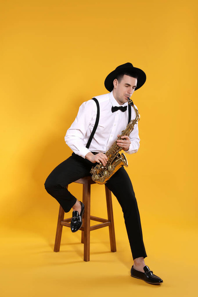 Young man in elegant outfit playing saxophone on yellow background - Fotografie, Obrázek