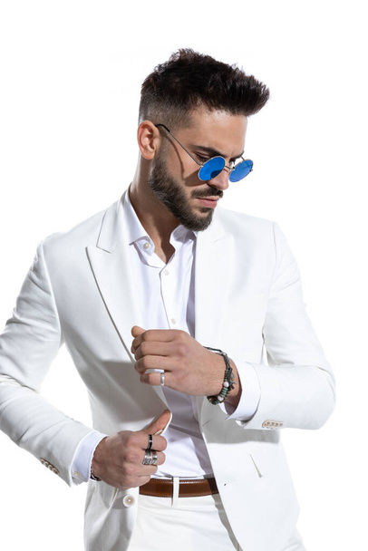 cool young man with retro sunglasses adjusting suit and looking away in a fashion light on white background in studio - Fotografie, Obrázek