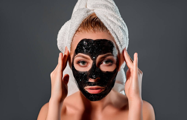 Schoonheid jong meisje met zwarte peel-off masker op haar gezicht. Foto van gelukkig meisje ontvangt spa behandeling op grijze achtergrond. Beauty & Skin care concept. - Foto, afbeelding