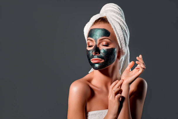 Portret van een mooi meisje met een groen masker op haar gezicht. Grijze achtergrond. Schoonheidsmeisje gezichtsverzorging. Cosmetologie, schoonheid en spa concept. - Foto, afbeelding