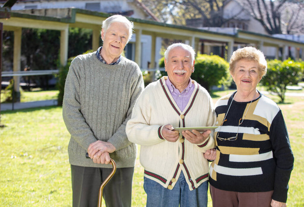 Biali seniorzy bawią się tabletkami na świeżym powietrzu. Emeryci i emeryci żyją swoim najlepszym życiem. - Zdjęcie, obraz