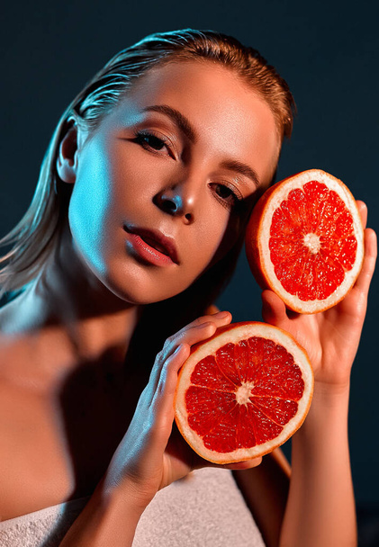 Great food for a healthy lifestyle. A beautiful young woman on a gray background holds a piece of grapefruit near her face. - Valokuva, kuva