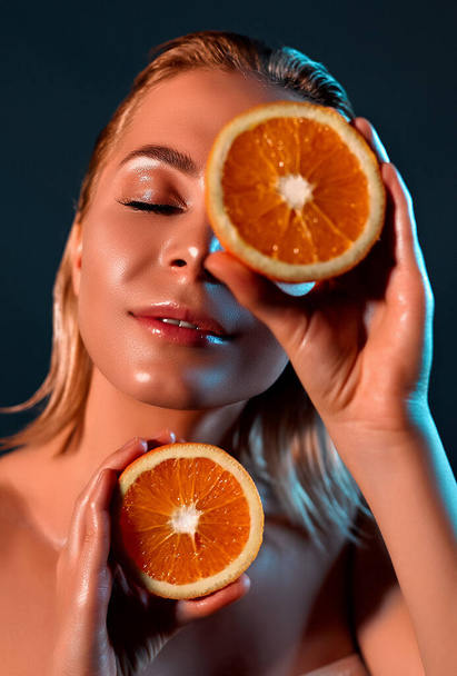 健康的なライフスタイルのための素晴らしい食品。灰色の背景の美しい若い女性は、彼女の目の前にオレンジの作品を保持しています. - 写真・画像