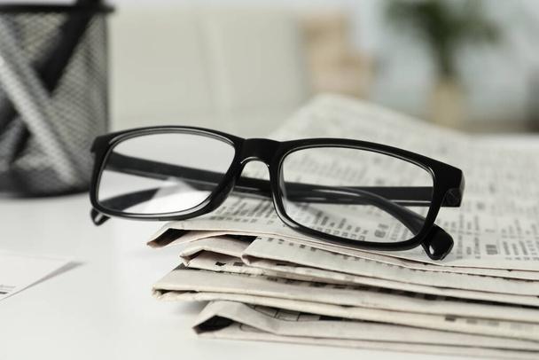 Stack of newspapers and glasses on white table indoors, closeup - Φωτογραφία, εικόνα