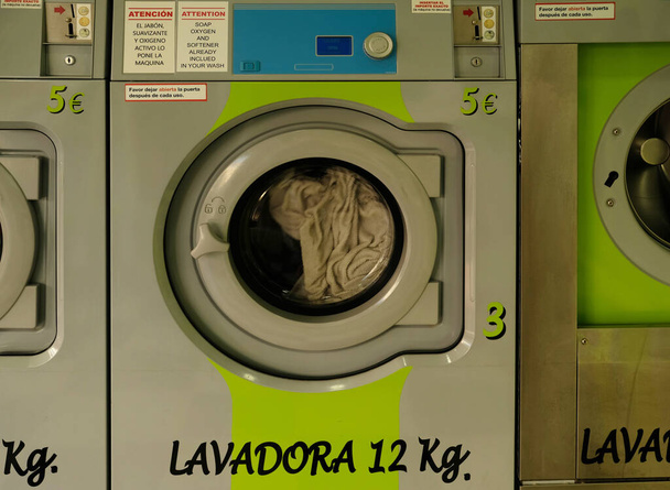 公共のセルフサービスのランドリーの緑のインテリア。コイン式洗濯機付き洗濯機。スペイン・アンダルシア州マラガ県のランドレットにある産業用洗濯機 - 写真・画像