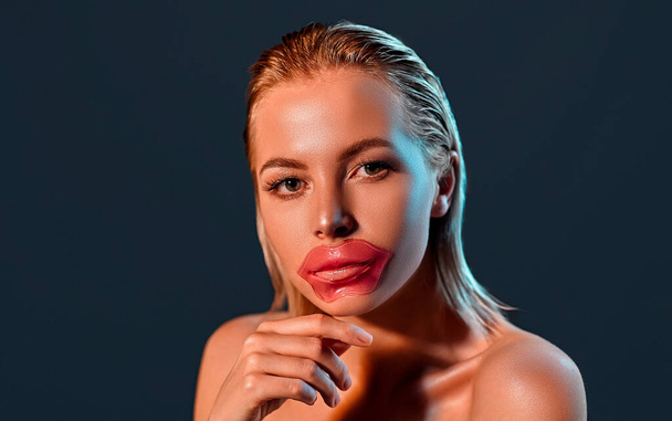 Retrato de una joven atractiva mujer rubia con la piel brillante con un parche de labio aislado sobre fondo gris. El concepto de cuidado de la piel, maquillaje. - Foto, Imagen