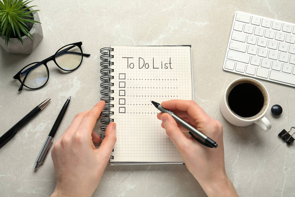 Woman filling To Do list in notepad at light grey marble table, top view - Photo, image