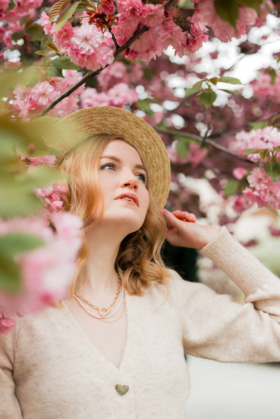 Mladá stylová žena stojící v sakura parku a vychutnat krásu růžové. Jarní žena v konceptu květu třešní. Krásná blondýnka s dlouhými vlasy venku. Třešňové květy. Zavřít portrét. - Fotografie, Obrázek