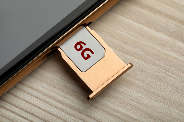 6G technology, Internet concept. SIM card in smartphone tray on wooden table, closeup - Фото, зображення