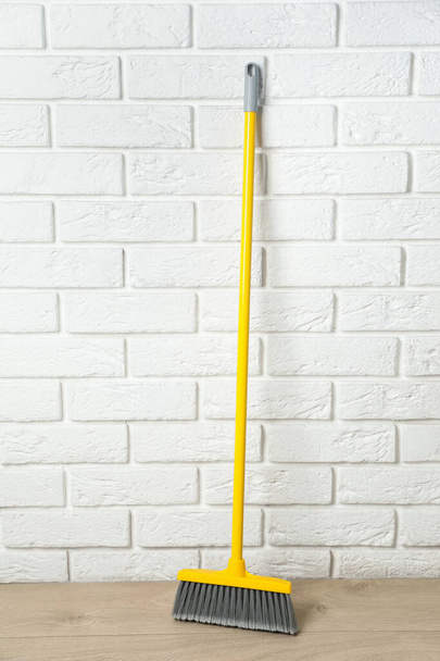 Plastic broom near white brick wall indoors - Valokuva, kuva