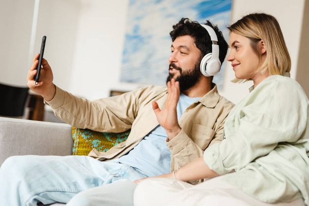 White couple using cellphone and gesturing while sitting on couch at home - Photo, image