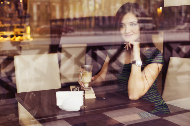 Brunette woman sitting at the cafe reading book, studing and drinking coffee and talking on the phone. Copy Space - Zdjęcie, obraz