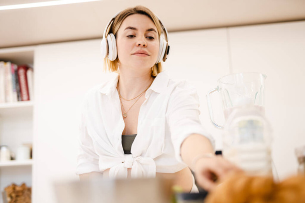 White pregnant woman in headphones making smoothy at home - Foto, imagen