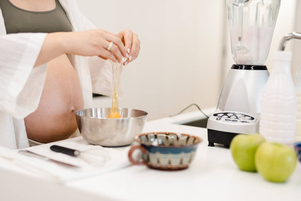 White pregnant woman cooking with eggs in kitchen at home - Fotó, kép