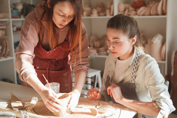 Досвідчений гончар навчає молоду жінку з глиною
 - Фото, зображення
