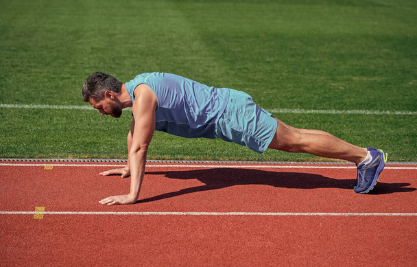male strength and power. sportsman in plank. athlete do pushups. train his core muscles. man doing push ups exercise on stadium. fitness gym outdoor. Working his core muscles - Photo, image