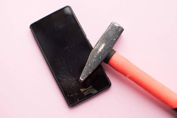 Hammer and mobile phone with broken display on pink background. Crashed smartphone concept. Top view. - Photo, Image