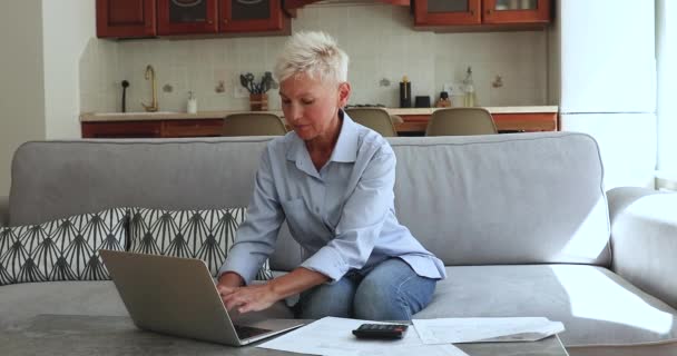 Older female using laptop paying bills through e-bank application - Materiał filmowy, wideo