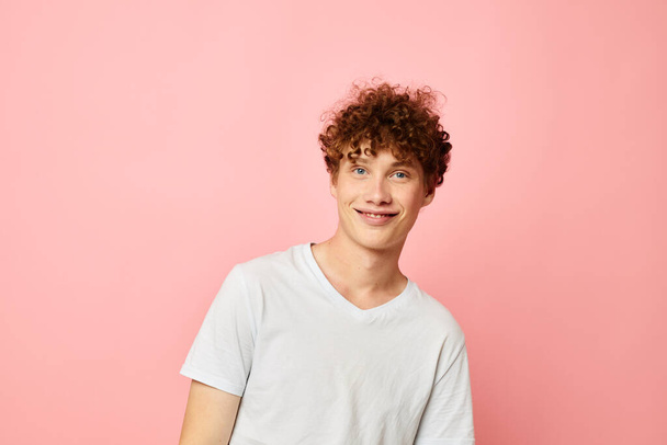 Young curly-haired man posing youth style white t-shirt pink background unaltered - Fotó, kép