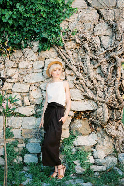 Giovane donna con un mazzo di lavanda si trova vicino a un muro di pietra intrecciato con edera - Foto, immagini