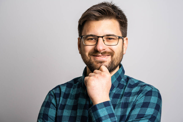 Retrato de un hombre caucásico adulto de 30 años con barba y anteojos mirando a la cámara frente al fondo blanco de la pared sonriendo usando espacio casual para copiar la camisa - Foto, Imagen