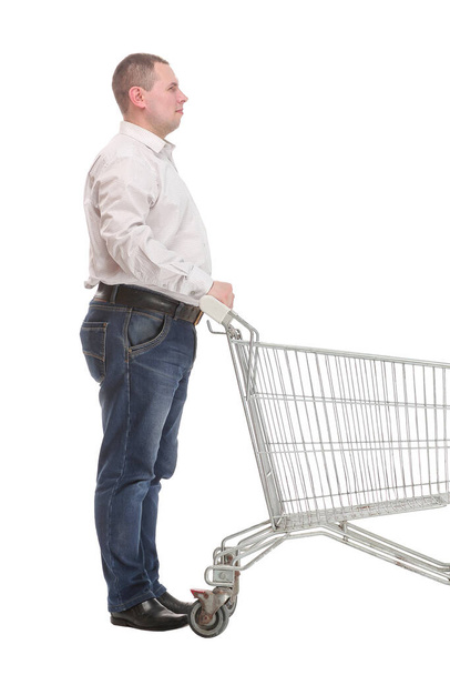 Full length side view of handsome young man standing with shopping trolley and looking at camera - Zdjęcie, obraz