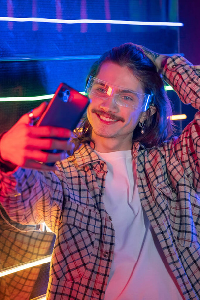 Человек с помощью смартфона и сделать селфи в ночном клубе с неоновым светом - Фото, изображение