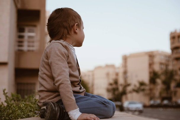 Pieni yksinäinen kadonnut poika 4-5-vuotias istuu kadulla ja katso tietä autolla - Valokuva, kuva