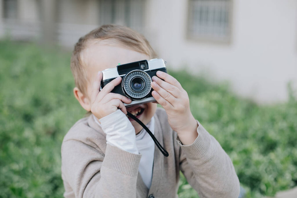 Kleiner glücklicher Junge hält Film analoge Vintage-Retro-Fotokamera, kleiner Fotograf schaut auf Sucher - Foto, Bild