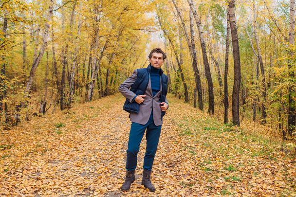 Tall handsome man dressed in a brown jacket walking in the autumn alley - Foto, Imagem
