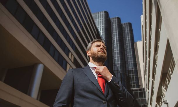 Businessman in blue suit tying the necktie outdoor. Well dressed business man on city office building. - Fotoğraf, Görsel