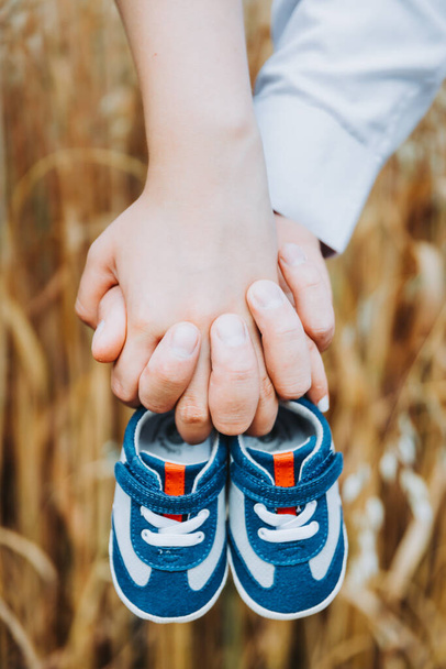Отцы и матери держат в руках маленькие детские туфельки. Концепция беременности - Фото, изображение
