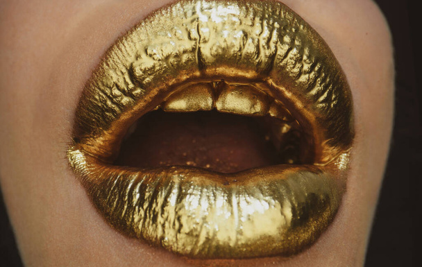 Gold lips. Gold paint from the open mouth. Golden lips on woman mouth with make-up. Sensual and creative design for golden metallic. - Photo, image