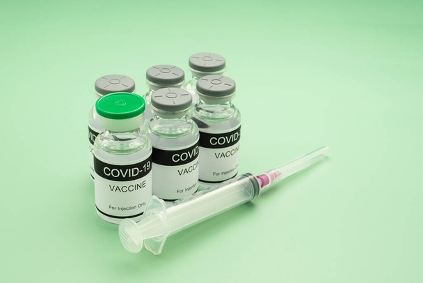 COVID-19 vaccine in glass bottles with a syringe placed on a green background. Vaccine for immunization, and treatment from coronavirus infection. Concept of medical and healthcare. - Foto, immagini