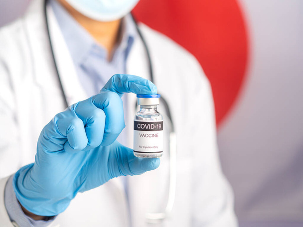 A doctor holding a COVID-19 vaccine bottle prepares vaccination against the background of the Japanese flag. Vaccine for immunization and treatment from virus infection. Medical concept. - Foto, Bild