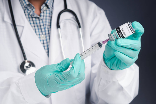 Um médico segurando uma seringa e um frasco de vacina COVID-19. Vacina para imunização e tratamento da infecção por coronavírus. Vista frontal. Conceito de médico e a luta contra o coronavírus. - Foto, Imagem