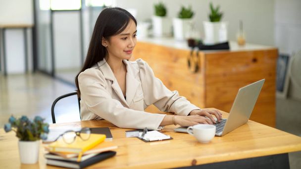Atrakcyjna Azjatka młoda bizneswoman zdalnie pracująca w kawiarni, pracująca na przenośnym laptopie. - Zdjęcie, obraz