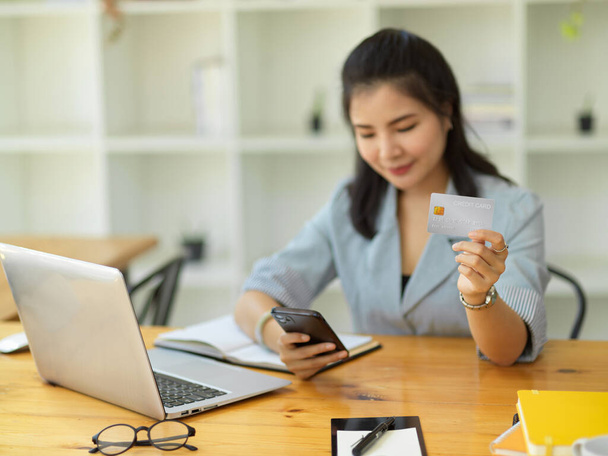 Взрослая азиатская бизнесвумен оплачивает счета в мобильном приложении, набирая номер своей кредитной карты в приложении интернет-банкинга. - Фото, изображение