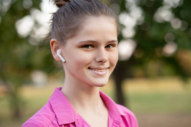 Piękna młoda dziewczyna słucha muzyki ze słuchawką z poczuciem szczęścia i relaksu w parku - Zdjęcie, obraz