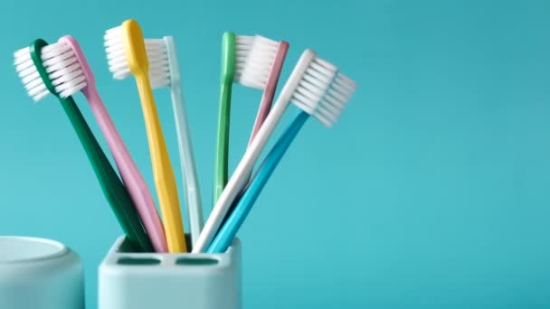  cepillos de dientes coloridos en taza blanca contra fondo verde claro  - Imágenes, Vídeo