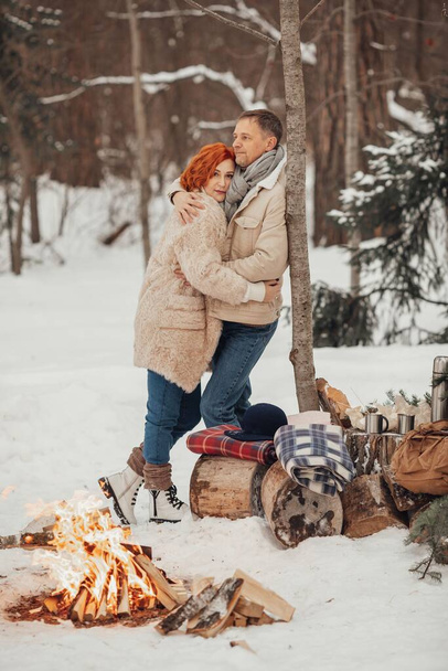 Una pareja enamorada, un hombre y una mujer en un bosque de invierno alrededor de una fogata toman café y dan malvaviscos. Foto de alta calidad - Foto, imagen