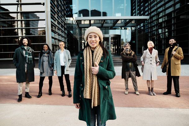 Geschäftsfrau hebt sich von einer vielfältigen Gruppe von Geschäftsleuten ab, während sie gemeinsam vor dem Bürogebäude posiert. - Foto, Bild